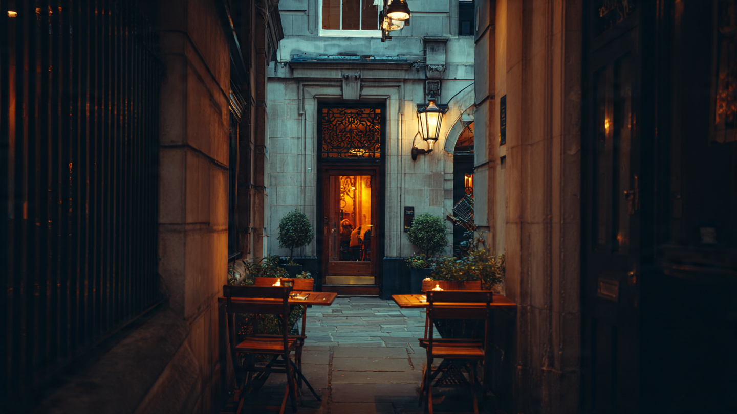 Romantic outdoor seating at one of the hidden cafes in London, tucked inside a narrow historic alley with warm lantern lighting and a cozy secret coffee spot atmosphere at night.