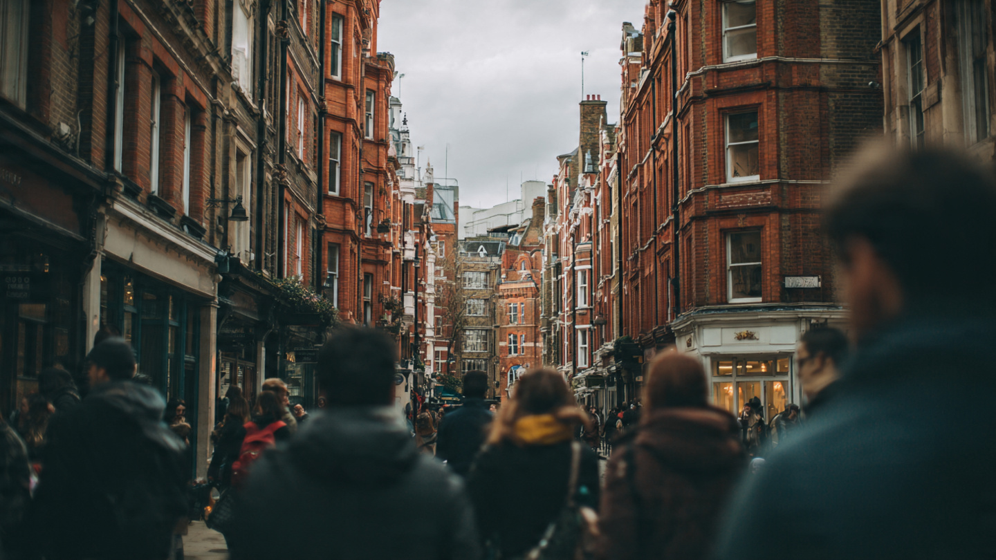 London weather travel guide showing pedestrians walking through a historic London street under cloudy skies