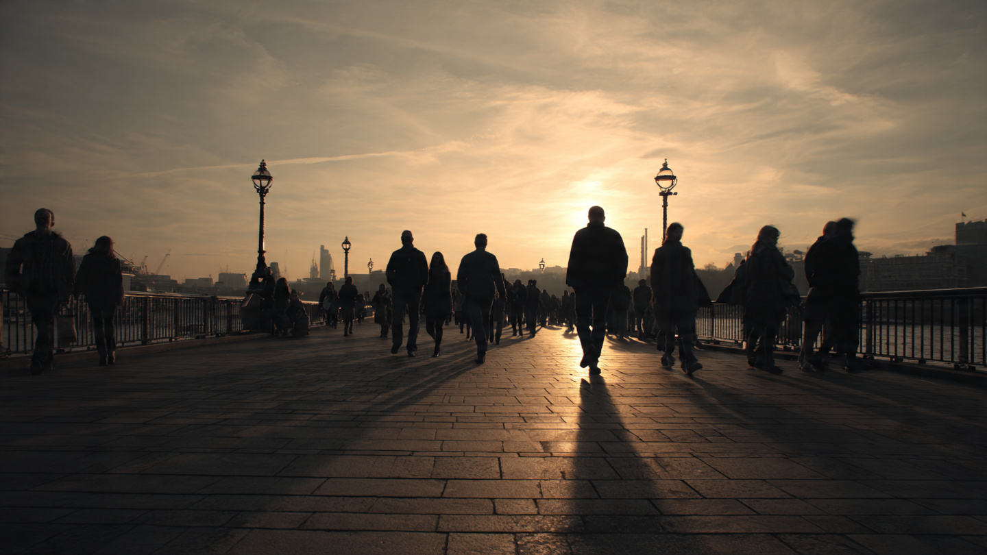 London weather travel guide showing pedestrians walking along a riverside path at sunset with long daylight shadows